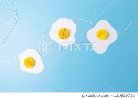 three fried eggs paper craft hanging from a string on a blue background, easter decoration concept,  120629736