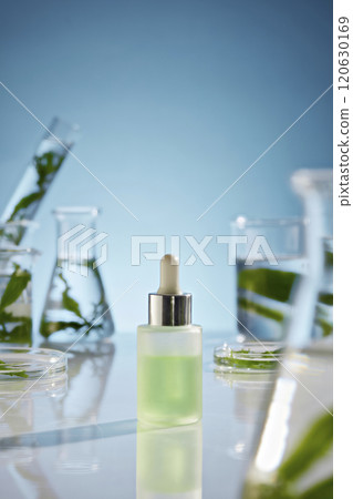 A serum bottle contains green liquid placed in center of white lab table, from frontal shot. On both sides displaying variety experiment utensils with fresh seaweed in A serum bottle contains green liquid placed in center of white lab table, from frontal shot. On both sides displaying variety experiment utensils with fresh seaweed in 120630169