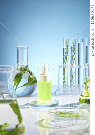 Minimal scene of experiment theme for advertising on backlit blue background. A blank label serum bottle of green liquid surrounded with experimental flasks filled seaweed leaves and clear liquid 120630173