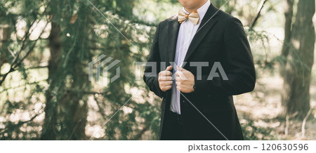 A man in a suit and bow tie standing under a tree in a park 120630596
