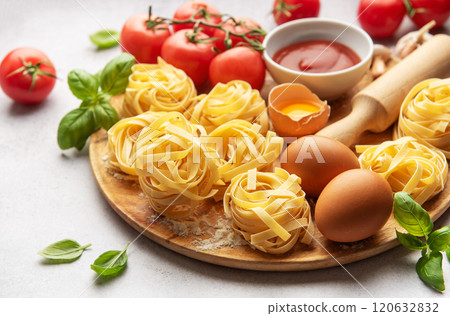 Fresh tagliatelle pasta nests with tomatoes, basil, eggs, flour and tomato sauce on wooden board Fresh tagliatelle pasta nests with tomatoes, basil, eggs, flour and tomato sauce on wooden board 120632832