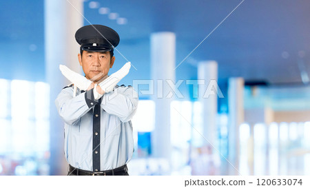 A male security guard showing a cross sign with his hand in the building's corridor 120633074
