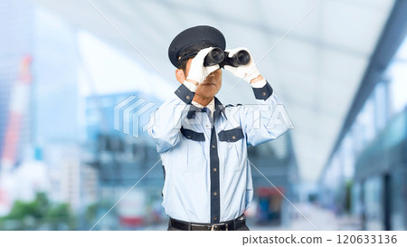 A male security guard looking around with binoculars in front of a city station 120633136