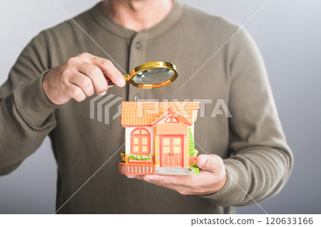 Homeowner holds a house model and uses a magnifying glass to inspect it, symbolizing the careful search for the perfect location for a new home. Reflects the thoughtfulness in choosing a dream home Homeowner holds a house model and uses a magnifying glass to inspect it, symbolizing the careful search for the perfect location for a new home. Reflects the thoughtfulness in choosing a dream home 120633166