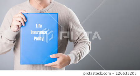 A man holds a blue life insurance policy booklet against a gray background, symbolizing the importance of planning and securing financial protection for the future 120633205