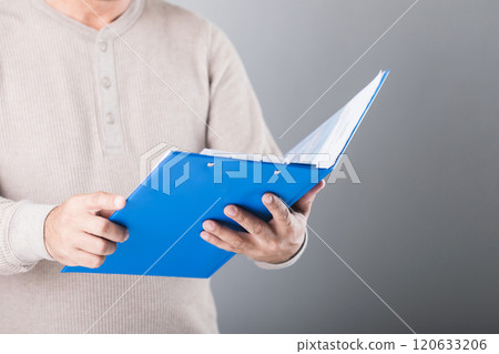 Man holds a blue life insurance policy booklet, reading and reviewing its details against a gray background. This image highlights the importance of understanding and planning financial security 120633206