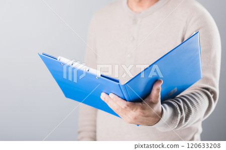 Man holds a blue life insurance policy booklet, reading and reviewing its details against a gray background. This image highlights the importance of understanding and planning financial security 120633208