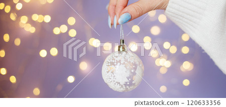 womans hands holding Christmas toy ball on purple blurred bokeh background womans hands holding Christmas toy ball on purple blurred bokeh background 120633356