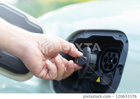 Car owner's hand grips the rubber cap of an electric vehicle charger, preparing to open or close it after use. Proper handling and maintenance in the use of clean energy charging solutions 120633376