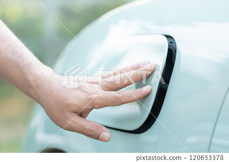 A car owner's hand gently touches the charging port cover of an electric vehicle, either opening or closing it after charging. Importance of proper handling in electric vehicle maintenance A car owner's hand gently touches the charging port cover of an electric vehicle, either opening or closing it after charging. Importance of proper handling in electric vehicle maintenance 120633378