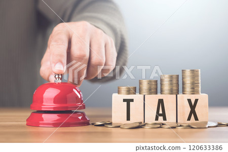 Hand presses a red bell beside a stack of coins on a wooden block labeled TAX, An urgent call to address tax matters and financial planning, Timely tax payments and financial responsibility Hand presses a red bell beside a stack of coins on a wooden block labeled TAX, An urgent call to address tax matters and financial planning, Timely tax payments and financial responsibility 120633386