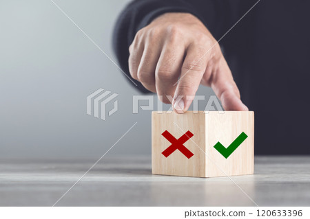 A man choosing between a checkmark and an 'X' symbol on wooden blocks. Image represents the concept of making the right choice, highlighting the importance of distinguishing between right and wrong A man choosing between a checkmark and an 'X' symbol on wooden blocks. Image represents the concept of making the right choice, highlighting the importance of distinguishing between right and wrong 120633396