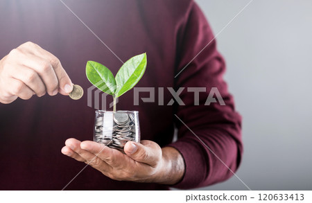 Businessman holds a coin jar with a sprouting plant, shielding it with his other hand. The gesture symbolizes nurturing and protecting personal finances for sustainable growth 120633413