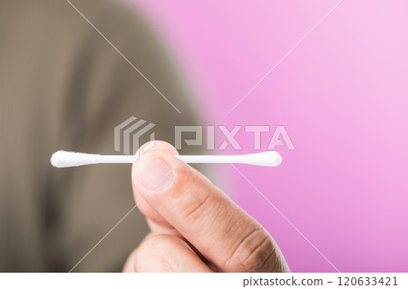 A close-up of a person holding a cotton swab against a pink background, highlighting the importance of correct usage and the recommendation to avoid reusing cotton swabs for hygiene A close-up of a person holding a cotton swab against a pink background, highlighting the importance of correct usage and the recommendation to avoid reusing cotton swabs for hygiene 120633421