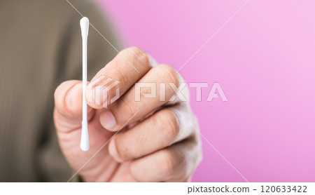 A close-up of a person holding a cotton swab against a pink background, highlighting the importance of correct usage and the recommendation to avoid reusing cotton swabs for hygiene A close-up of a person holding a cotton swab against a pink background, highlighting the importance of correct usage and the recommendation to avoid reusing cotton swabs for hygiene 120633422