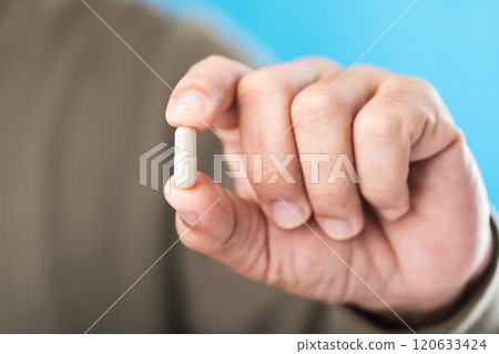 Close-up of a person holding a capsule against a blue background, emphasizing the importance of proper medication use and the reminder to read labels carefully before each dose Close-up of a person holding a capsule against a blue background, emphasizing the importance of proper medication use and the reminder to read labels carefully before each dose 120633424