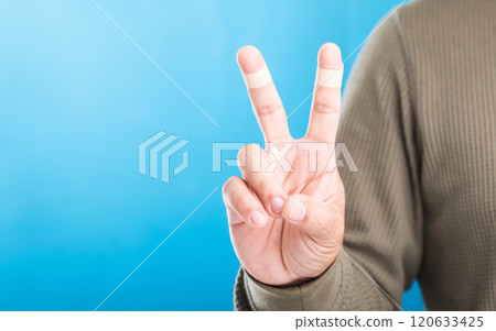 Hand with bandages or plaster on the index and middle fingers forming a 'V' sign, symbolizing resilience and the ability to keep working and going despite minor injuries Hand with bandages or plaster on the index and middle fingers forming a 'V' sign, symbolizing resilience and the ability to keep working and going despite minor injuries 120633425