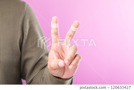 Hand with bandages or plaster on the index and middle fingers forming a 'V' sign, symbolizing resilience and the ability to keep working and going despite minor injuries Hand with bandages or plaster on the index and middle fingers forming a 'V' sign, symbolizing resilience and the ability to keep working and going despite minor injuries 120633427