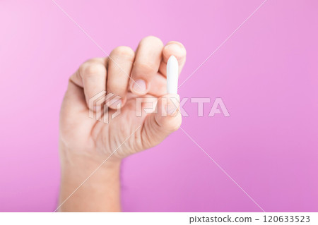 A hand holding a suppository for hemorrhoid treatment, symbolizing proactive health care and self-care. Set against a soft pink background, emphasizing the importance of managing health needs 120633523