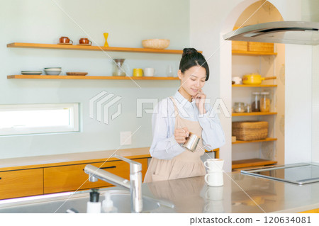 A woman in an apron standing in the kitchen 120634081