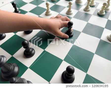Childs hand holding chess pawn on green and white chessboard 120634195