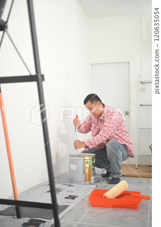 Young asian man wearing plaid shirt painting white wall in newly renovated room Young asian man wearing plaid shirt painting white wall in newly renovated room 120635054