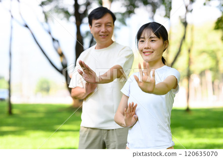 Middle aged father and his daughter are enjoying Tai Chi session together in a park Middle aged father and his daughter are enjoying Tai Chi session together in a park 120635070