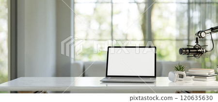 A laptop, headphones, and a microphone on a white table in a modern bright living room. 120635630