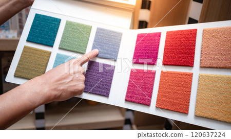 Designer hand pointing at sample fabric pieces on carpet swatch collection 120637224