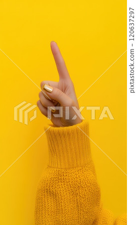Female hand in yellow sweater pointing up on yellow background 120637297