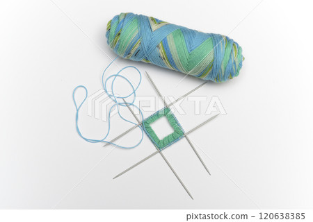 a skein of colorful variegated yarn in shades of blue, green, and yellow, alongside a small knitting project on four double-pointed needles 120638385