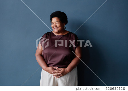 Minimal waist up portrait of kind African American senior woman standing against blue background in studio with soft natural light and copy space 120639128