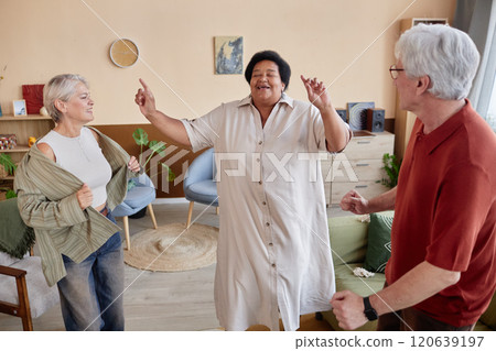 Candid scene with joyful senior Black woman dancing with friends in cozy living room indoors enjoying activities 120639197