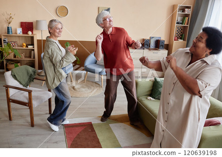 Full length view at group of joyful senior friends dancing together and listening to music enjoying entertainment in cozy living room Full length view at group of joyful senior friends dancing together and listening to music enjoying entertainment in cozy living room 120639198