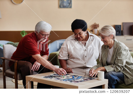 Group of elegant senior people playing board game together enjoying quiet entertainment indoors in cozy living room Group of elegant senior people playing board game together enjoying quiet entertainment indoors in cozy living room 120639207