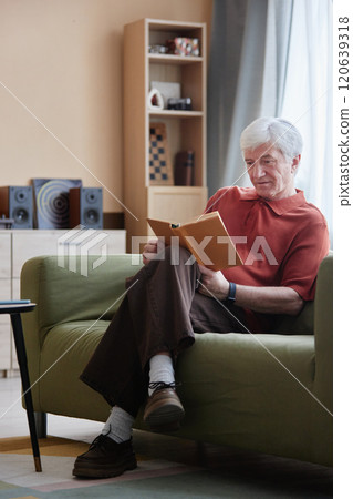 Vertical full length portrait of white haired senior man reading book sitting on sofa at home and enjoying quiet entertainment Vertical full length portrait of white haired senior man reading book sitting on sofa at home and enjoying quiet entertainment 120639318