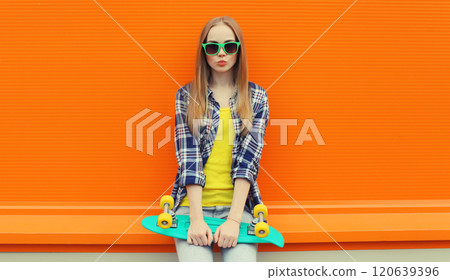 Summer portrait of happy cheerful stylish young woman with skateboard posing on orange background Summer portrait of happy cheerful stylish young woman with skateboard posing on orange background 120639396