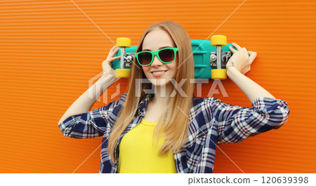 Summer portrait of happy cheerful stylish young woman with skateboard posing on orange background 120639398