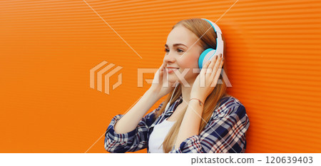 Summer portrait happy modern young woman listening to music with headphones on orange background 120639403
