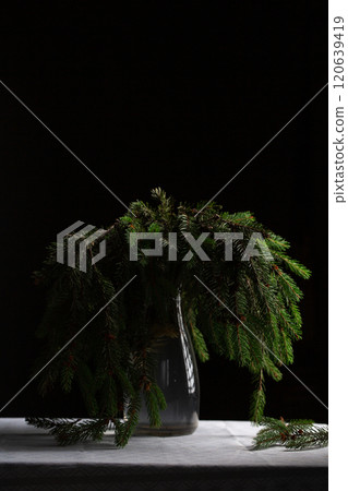A transparent vase with green fluffy branches of a Christmas tree stands on the table A transparent vase with green fluffy branches of a Christmas tree stands on the table 120639419