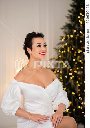 A woman in a white dress sits in front of a Christmas tree A woman in a white dress sits in front of a Christmas tree 120639468