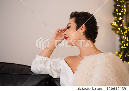 A woman is sitting on a couch with a white fur fur coat over her shoulders A woman is sitting on a couch with a white fur fur coat over her shoulders 120639489