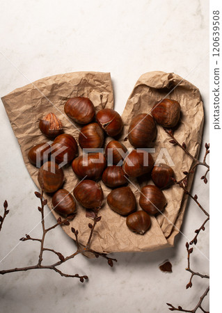Fresh harvest of edible chestnuts scattered on a on kraft paper with tree branches Fresh harvest of edible chestnuts scattered on a on kraft paper with tree branches 120639508