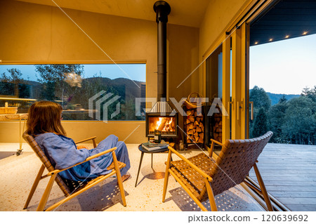 Woman in a blue lounge set sitting by the fireplace Woman in a blue lounge set sitting by the fireplace 120639692