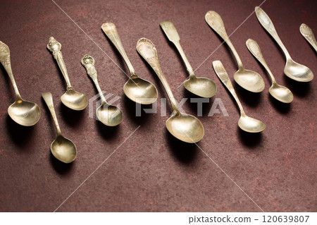 A collection of vintage spoons laid out in rows on a burgundy background 120639807