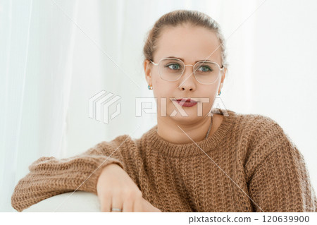 A woman wearing glasses and a brown sweater is sitting on a couch A woman wearing glasses and a brown sweater is sitting on a couch 120639900