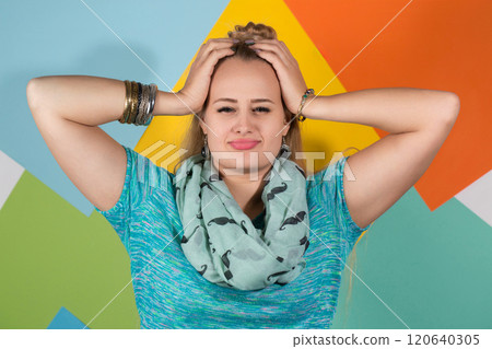 A woman in a turquoise T-shirt and a scarf holds her head with her hands 120640305