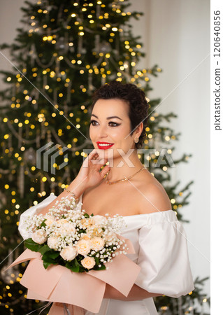 A woman is standing in front of a Christmas tree, holding a bouquet of flowers A woman is standing in front of a Christmas tree, holding a bouquet of flowers 120640856