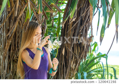 Woman holding a white flower of Plumeria in her hand against the ocean background 120641198