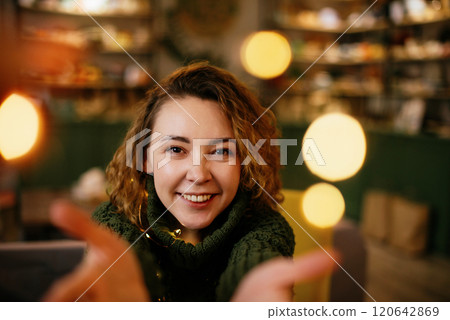 Festive holiday scene of a woman glowing with joy, surrounded by Christmas and New Year lights. Smiling middle-aged woman enjoying cozy Christmas and New Year holidays 120642869
